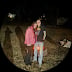 Two people standing together at night in a natural outdoor setting with trees and foliage