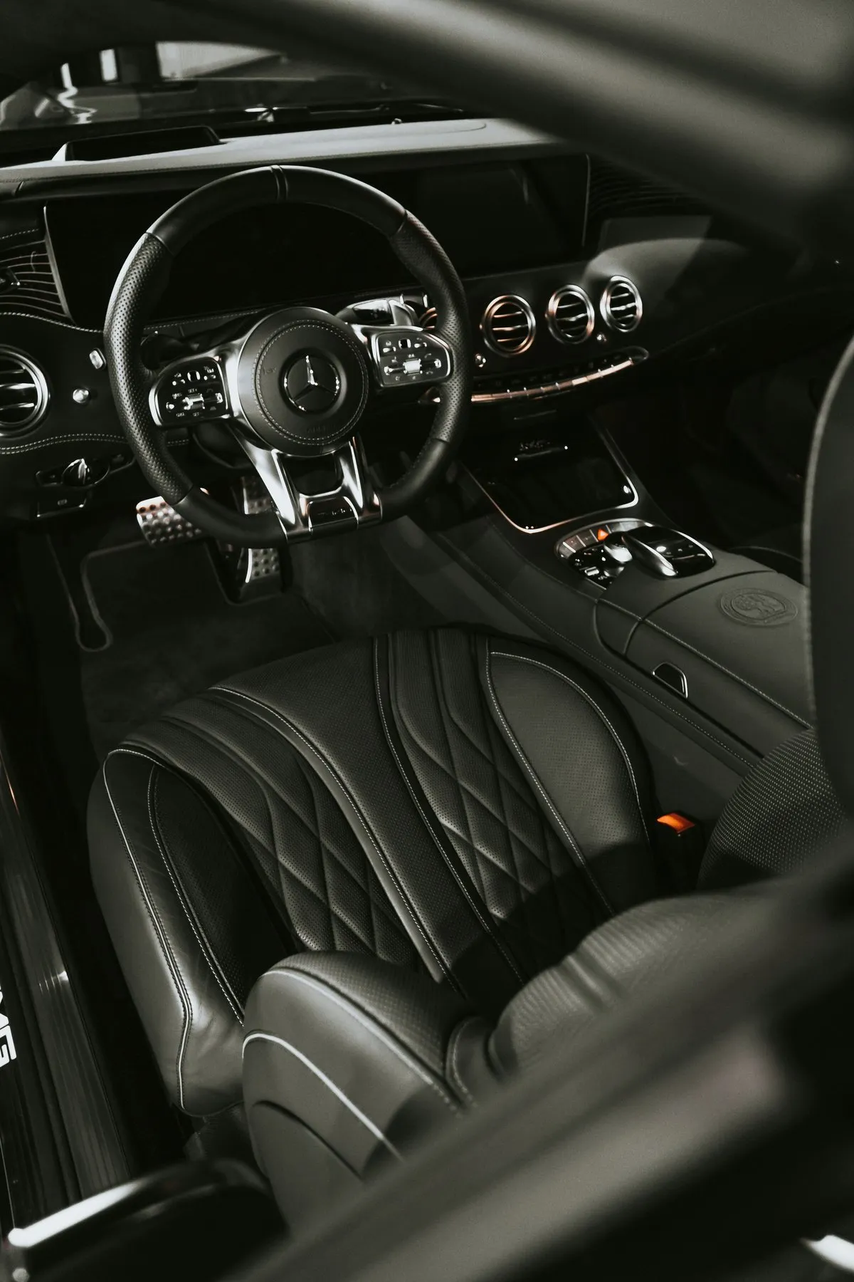 Black luxury car interior with leather steering wheel, quilted seats and illuminated dashboard